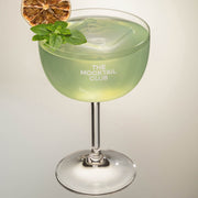 Mocktail glass filled with ice cubes, Basil Breeze mocktail, finished with Greek basil and a slice of dried lime