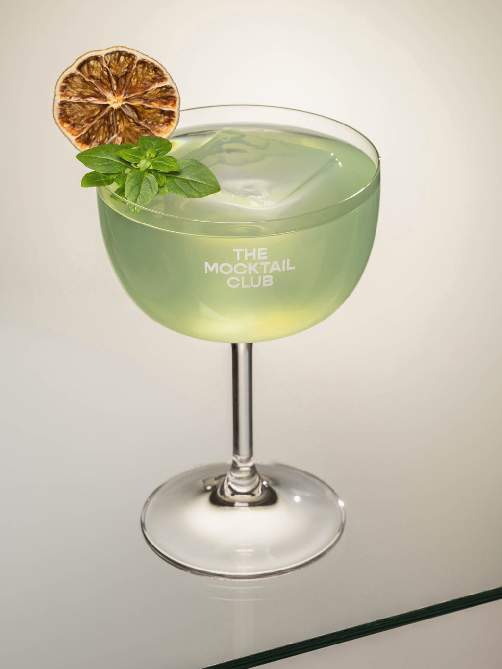 Mocktail glass filled with ice cubes, Basil Breeze mocktail, finished with Greek basil and a slice of dried lime