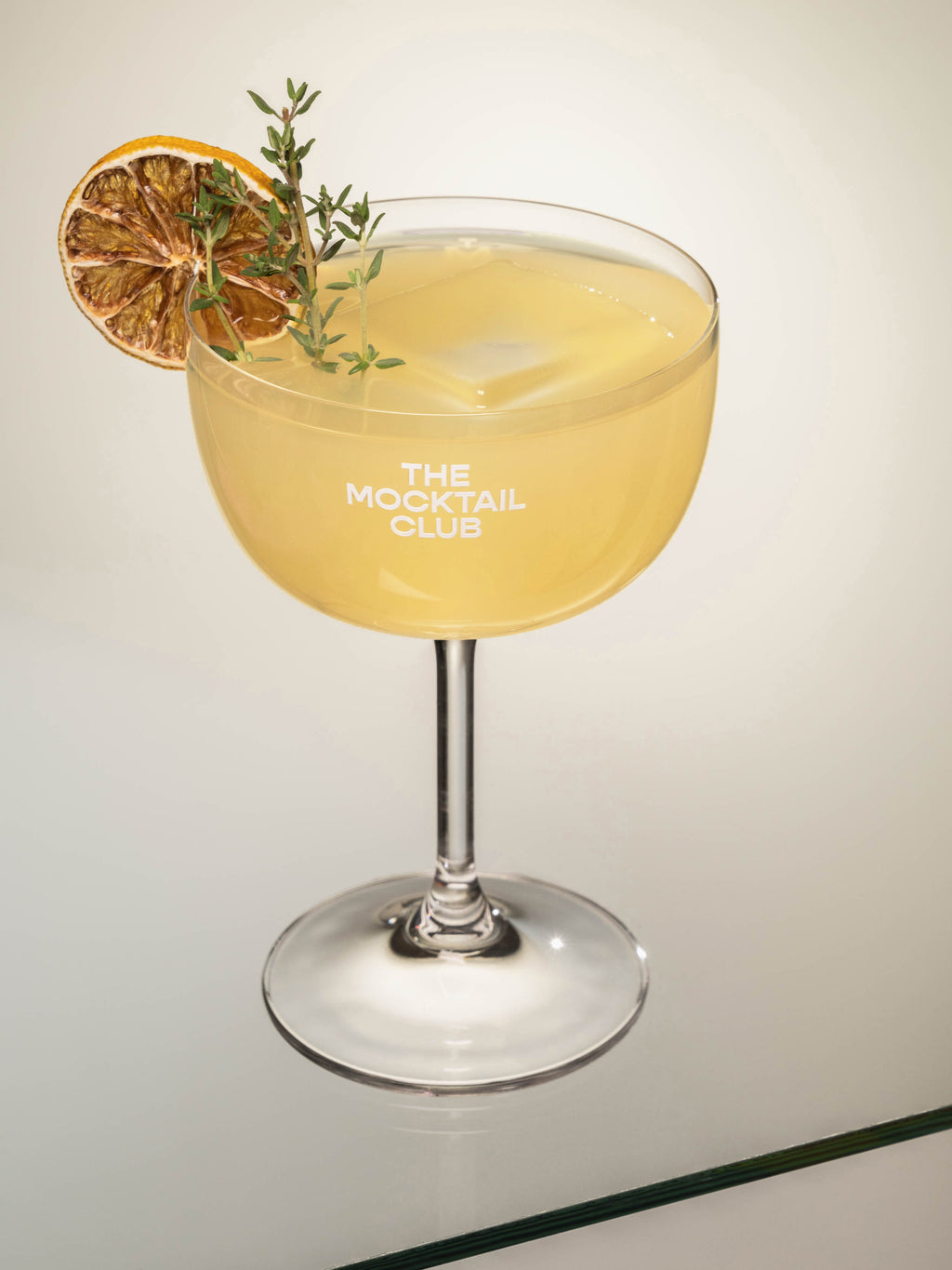 Mocktail glass filled with ice cubes, Ginger Gem mocktail, finished with thyme and a slice of dried lime 