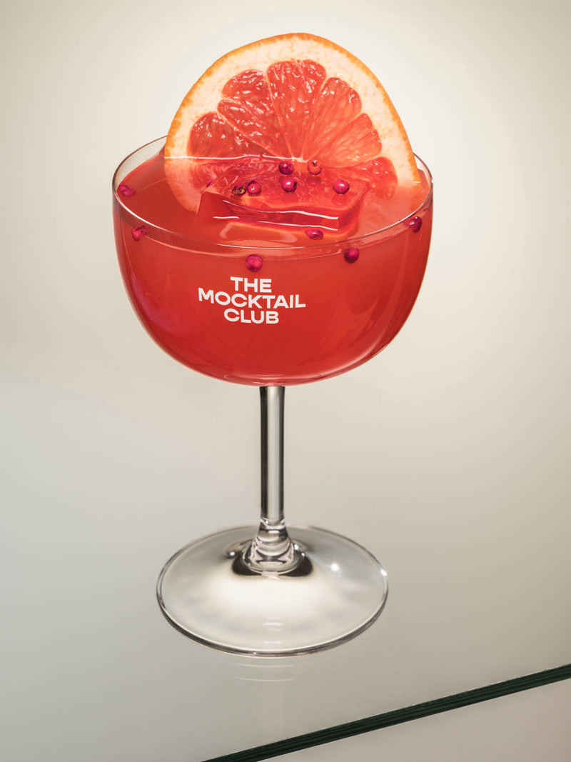 Mocktail glass filled with ice cubes, Grapefruit Grace mocktail, finished with pink peppercorns and a slice of grapefruit 